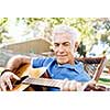Handsome senior man playing guitar in summer park