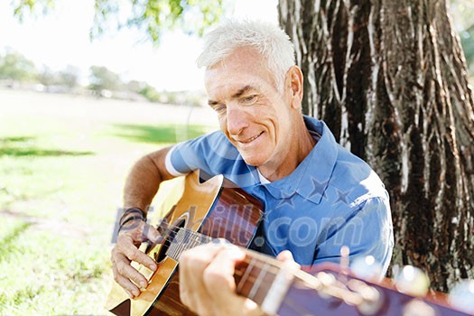 Handsome senior man playing guitar in summer park Handsome senior man playing guitar in summer park