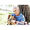 Handsome senior man playing guitar in summer park