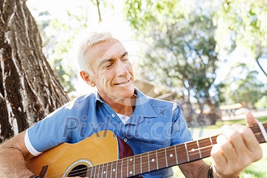 Handsome senior man playing guitar in summer park Handsome senior man playing guitar in summer park