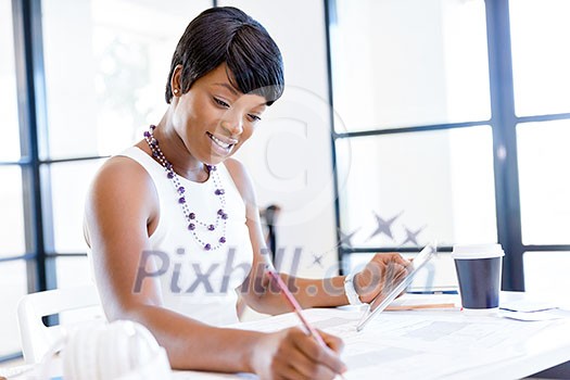 Young beautiful woman sitting at a desk in an office and working on blueprint Young beautiful woman sitting at a desk in an office and working on blueprint