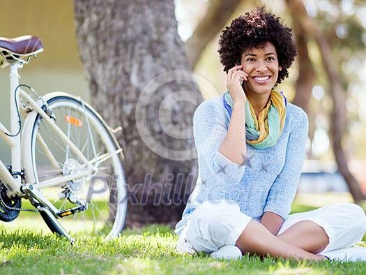 Charming young woman sitting in summer park and holding mobile phone Charming young woman sitting in summer park and holding mobile phone
