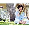 Charming young woman sitting in summer park and holding mobile phone