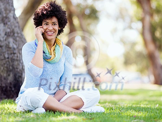 Charming young woman sitting in summer park and holding mobile phone Charming young woman sitting in summer park and holding mobile phone