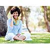 Charming young woman sitting in summer park and holding mobile phone