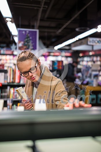 Pretty, young female choosing a good book to buy in a bookstore Pretty, young female choosing a good book to buy in a bookstore