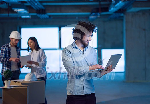young male architect on construction site checking documents and business workflow using laptop computer with colleagues in the background in new startup office young male architect on construction site checking documents and business workflow using laptop computer with colleagues in the background in new startup office