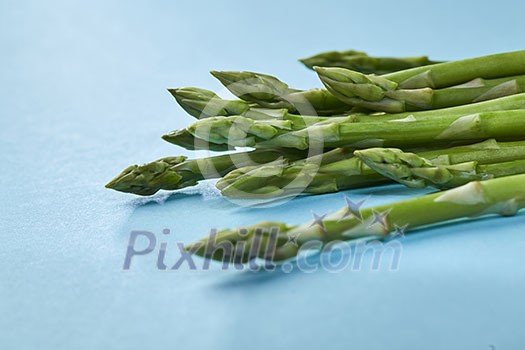 Organic green asparagus in a bunch ready to cook healthy vegetarian food on blue background. Organic green asparagus in a bunch ready to cook healthy vegetarian food on blue background.