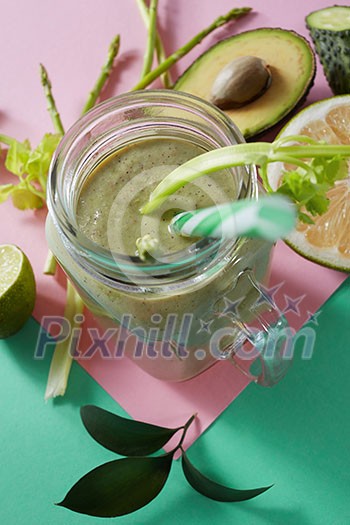 Vegetarian healthy smoothies from green vegetables with green leaves, slices of lemon, avocado, cocumber and plastic straw in a glass bowl on duotone pink green paper background. Vegetarian healthy smoothies from green vegetables with green leaves, slices of lemon, avocado, cocumber and plastic straw in a glass bowl on duotone pink green paper background.
