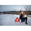 Young woman setting up a warning triangle and calling for assistance after her car broke down in the middle of nowhere on a freezing winter day