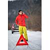 Young man setting up a warning triangle and calling for assistance after his car broke down in the middle of nowhere on a freezing winter day