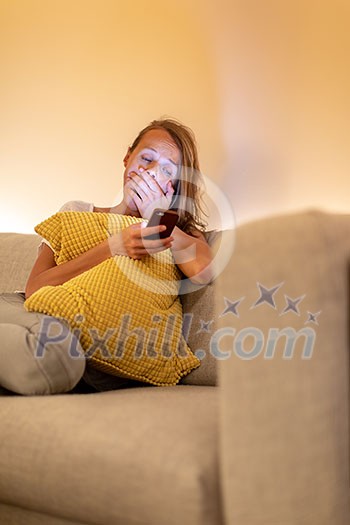 Cute young woman on a comfortable sofa in her modern apartment using her cell phone