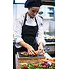 female Chef  in hotel or restaurant kitchen preparing beef steak with vegetable decoration