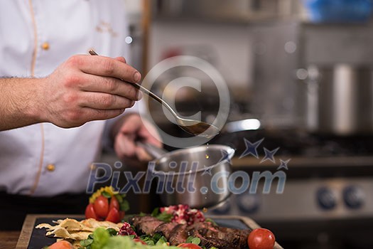Chef hand finishing steak meat plate with Finally dish dressing and almost ready to serve at the table Chef hand finishing steak meat plate with Finally dish dressing and almost ready to serve at the table