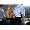 Young male chef flipping vegetables in wok at commercial kitchen