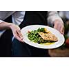 Chef hands holding fried Salmon fish fillet with vegetables for dinner in a restaurant kitchen