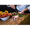 Master Chef hands putting salt on juicy slice of raw steak with vegetables around on a wooden table