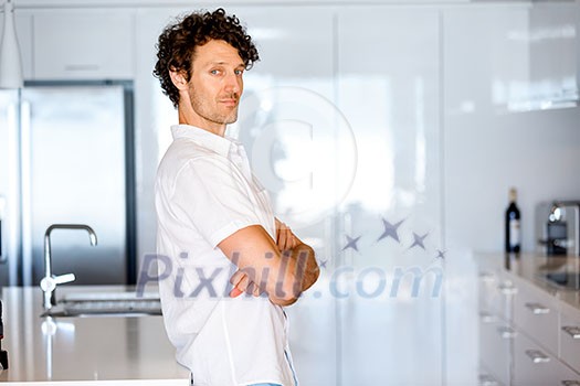 Portrait of a smart young man with curly hair standing in kitchen Portrait of a smart young man with curly hair standing in kitchen