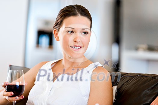 Beautiful young woman holding glass with red wine and smiling while sitting Beautiful young woman holding glass with red wine and smiling while sitting