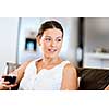 Beautiful young woman holding glass with red wine and smiling while sitting