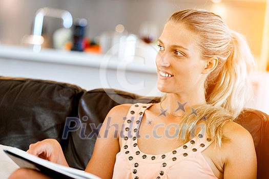Happy woman reading a magazine sitting on a sofa in the living room at home Happy woman reading a magazine sitting on a sofa in the living room at home