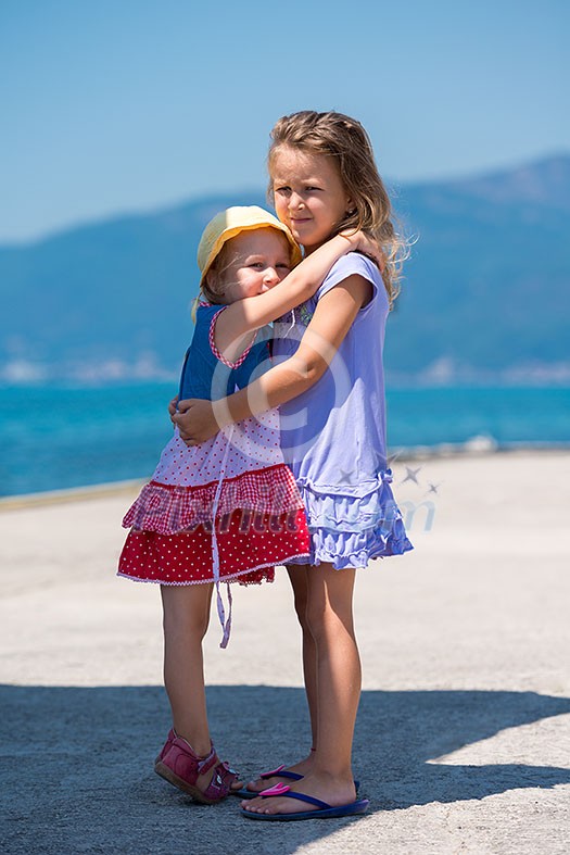 Happy smiling little sisters having fun while hugging on the beach coast during Summer vacation Healthy childhood lifestyle concept Happy smiling little sisters having fun while hugging on the beach coast during Summer vacation Healthy childhood lifestyle concept