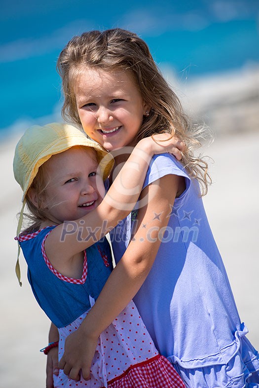 Happy smiling little sisters having fun while hugging on the beach coast during Summer vacation Healthy childhood lifestyle concept Happy smiling little sisters having fun while hugging on the beach coast during Summer vacation Healthy childhood lifestyle concept