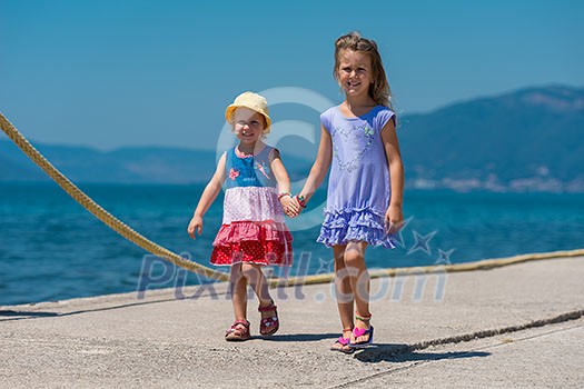 Happy smiling little sisters having fun holding their hands while walking on the beach coast during Summer vacation Healthy childhood lifestyle concept Happy smiling little sisters having fun holding their hands while walking on the beach coast during Summer vacation Healthy childhood lifestyle concept