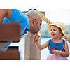 cute little girl having fun with her young father while eating ice cream by the sea during summer vacation holidays, celebration, children and people concept