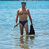 Young smiling fisherman with equipment standing in the shallow water of the sea while preparing for underwater fishing  active holiday concept