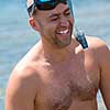 Young smiling fisherman with equipment standing in the shallow water of the sea while preparing for underwater fishing  active holiday concept