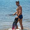 Young smiling fisherman with equipment standing in the shallow water of the sea while preparing for underwater fishing  active holiday concept