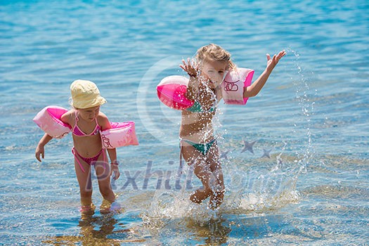 two happy little girls with swimming armbands playing in shallow water of the sea during Summer vacation Healthy childhood lifestyle concept two happy little girls with swimming armbands playing in shallow water of the sea during Summer vacation Healthy childhood lifestyle concept