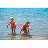 two happy little girls with swimming armbands playing in shallow water of the sea during Summer vacation  Healthy childhood lifestyle concept