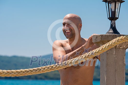 Portrait of a young smiling muscular man with naked torso while standing on the coast by the sea Portrait of a young smiling muscular man with naked torso while standing on the coast by the sea