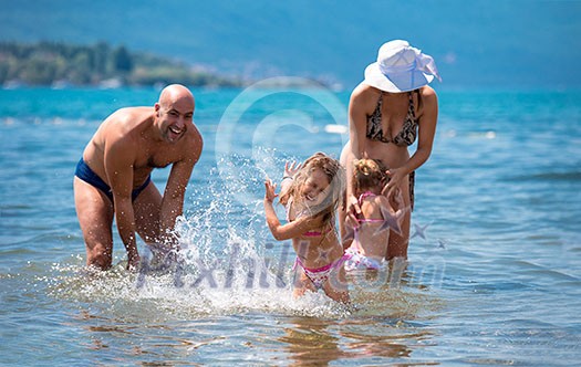 young happy couple with cute little daughters having fun while splashing each other in the shallow water of the sea during Summer vacation Healthy family holiday concept young happy couple with cute little daughters having fun while splashing each other in the shallow water of the sea during Summer vacation Healthy family holiday concept