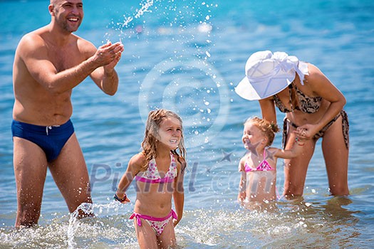 young happy couple with cute little daughters having fun while splashing each other in the shallow water of the sea during Summer vacation Healthy family holiday concept young happy couple with cute little daughters having fun while splashing each other in the shallow water of the sea during Summer vacation Healthy family holiday concept