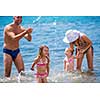 young happy couple with cute little daughters having fun while splashing each other in the shallow water of the sea during Summer vacation  Healthy family holiday concept