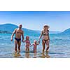 portrait of a young happy couple with cute little daughters having fun while standing in the shallow water of the sea during Summer vacation  Healthy family holiday concept