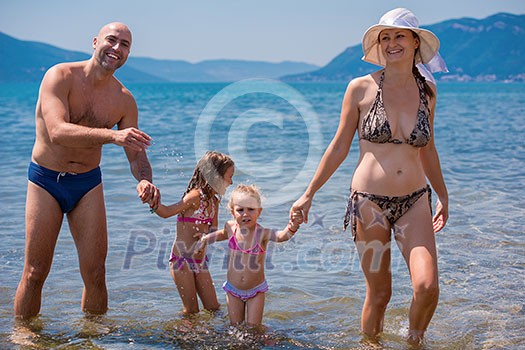 portrait of a young happy couple with cute little daughters having fun while standing in the shallow water of the sea during Summer vacation Healthy family holiday concept portrait of a young happy couple with cute little daughters having fun while standing in the shallow water of the sea during Summer vacation Healthy family holiday concept