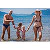 portrait of a young happy couple with cute little daughters having fun while standing in the shallow water of the sea during Summer vacation  Healthy family holiday concept