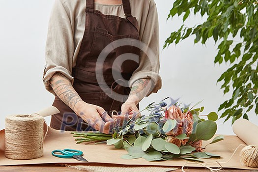 Girl's florist hands with tatoo are making bouquet with fresh flowers roses living coral color at the table with paper and rope. Process step by step. Concept floral shop. Girl's florist hands with tatoo are making bouquet with fresh flowers roses living coral color at the table with paper and rope. Process step by step. Concept floral shop.