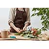 Girl's florist hands with tatoo are making bouquet with fresh flowers roses living coral color at the table with paper and rope. Process step by step. Concept floral shop.