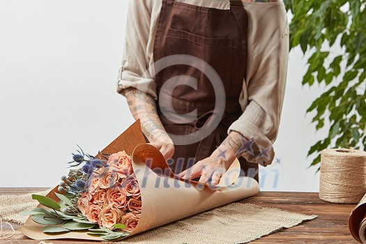 Girl's florist hands with tatoo are making bouquet with fresh flowers roses living coral color at the table with paper and rope. Process step by step. Concept floral shop. Girl's florist hands with tatoo are making bouquet with fresh flowers roses living coral color at the table with paper and rope. Process step by step. Concept floral shop.
