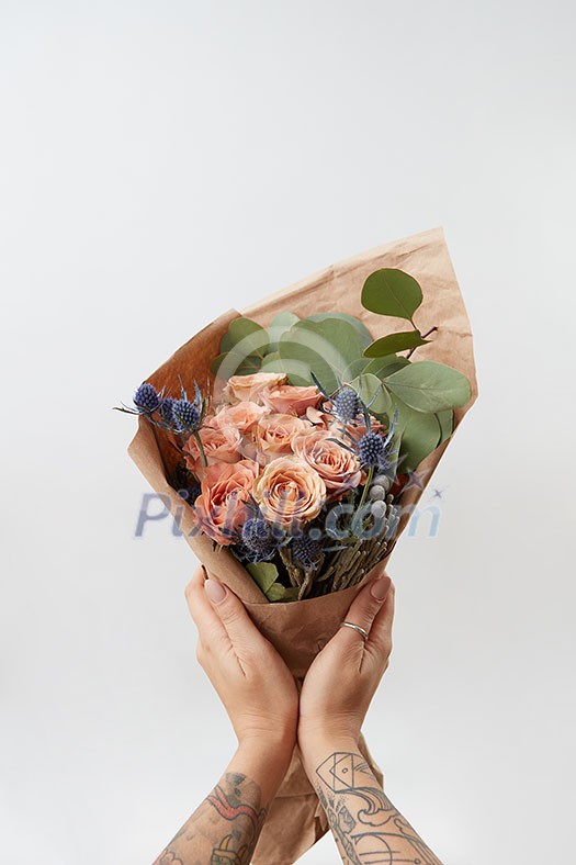 Spring wonderful fresh roses, eryngium and green leaves as a greeting bunch in a girl's hands with tattoo on a light background. Place for text. Gift for Mother's Day. Spring wonderful fresh roses, eryngium and green leaves as a greeting bunch in a girl's hands with tattoo on a light background. Place for text. Gift for Mother's Day.