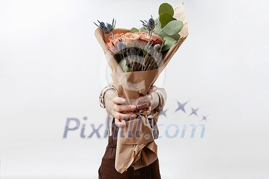 Delicate flowers living coral roses and eryngium as a beautiful bouquet in girl's hands on a gray background. Place for text. Congratulation card for Woman's or Mother's Day. Delicate flowers living coral roses and eryngium as a beautiful bouquet in girl's hands on a gray background. Place for text. Congratulation card for Woman's or Mother's Day.