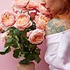 Wonderful summer fresh roses living coral colored as a greeting bouquet in a female's hand with tattoo on a coral background. Place for text. Gift for Mother's Day.