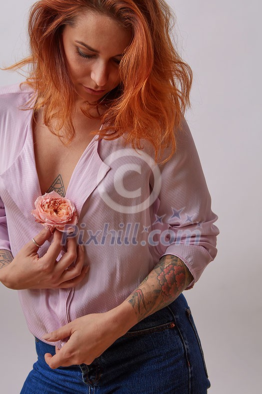 Pretty woman with ginger hair, tattoo on her bust and hands holds fresh rose living coral color on a light background. Copy space. Postcard for Woman's or Mother's Day. Pretty woman with ginger hair, tattoo on her bust and hands holds fresh rose living coral color on a light background. Copy space. Postcard for Woman's or Mother's Day.