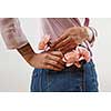 Young girl wearing of jeans pants and pink shirt from back put in natural flowers roses in a pocket on a gray background, place for text. Concept of Woman's or Mother's Day.
