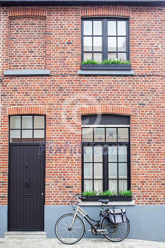 Bruges, Belgium - August 16, 2013: Vintage bike with a bag against the wall with a dark door and windows on the street of Bruges on a summer day Bruges, Belgium - August 16, 2013: Vintage bike with a bag against the wall with a dark door and windows on the street of Bruges on a summer day